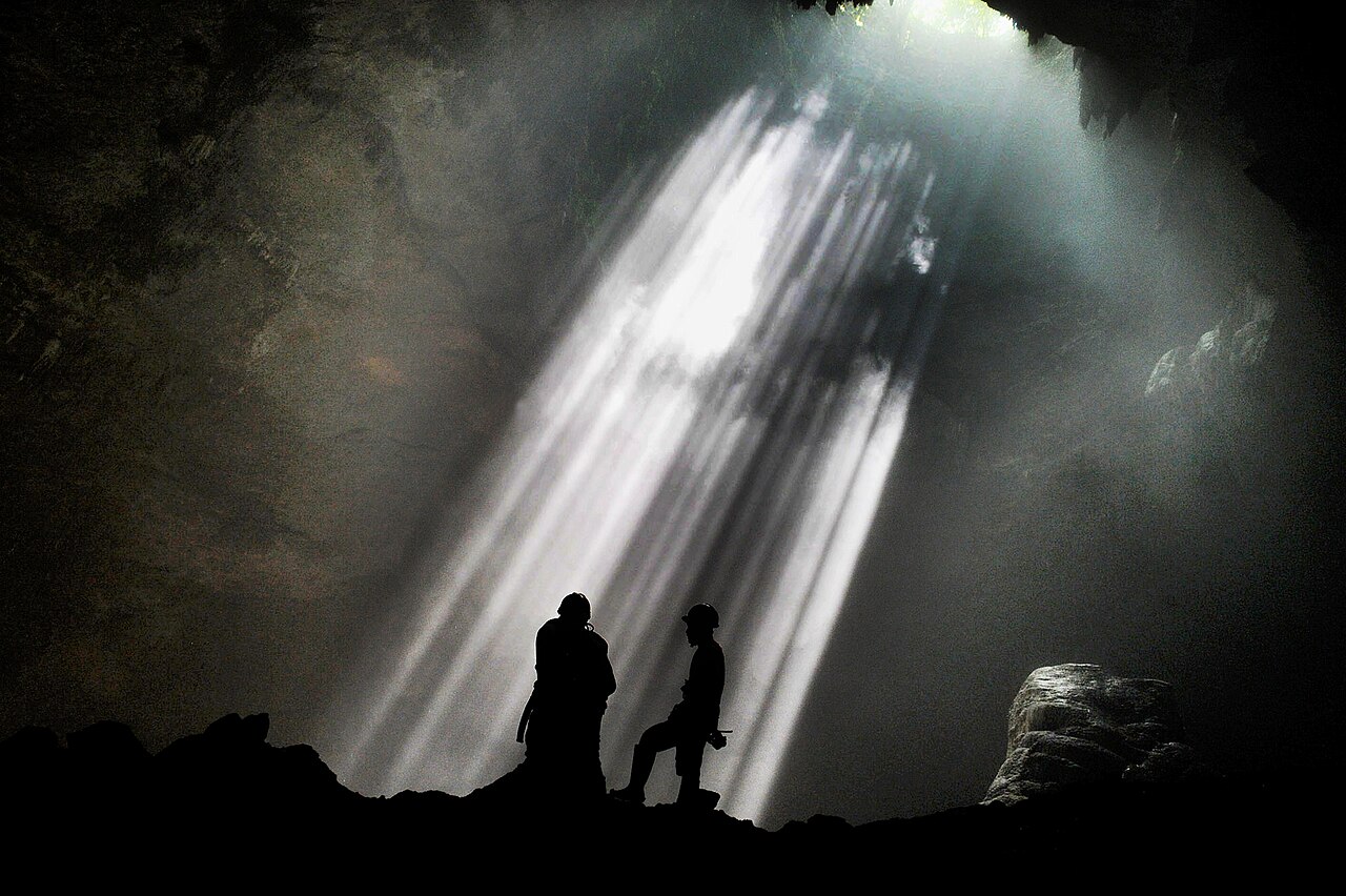 Rayons de lumière dans la grotte de Jomblang, spéléologues en contre-jour